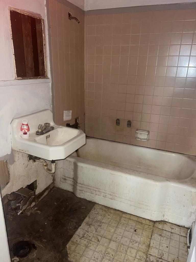Original bathroom with pink tile, rusted fixtures and rotted flooring