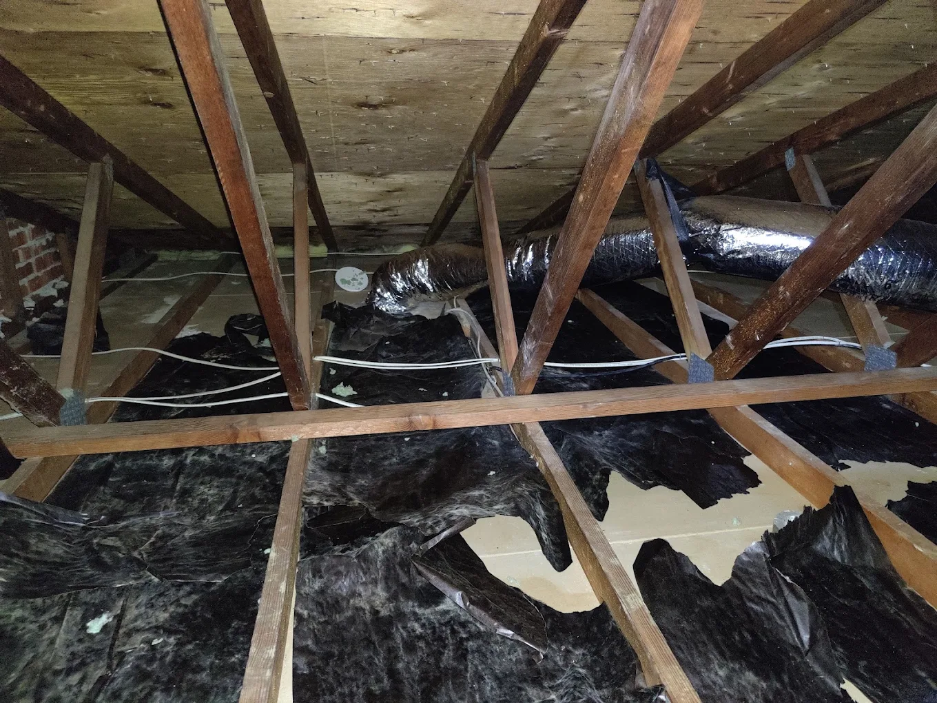 Attic before: shredded black vapor barrier, exposed joists, bare drywall showing through