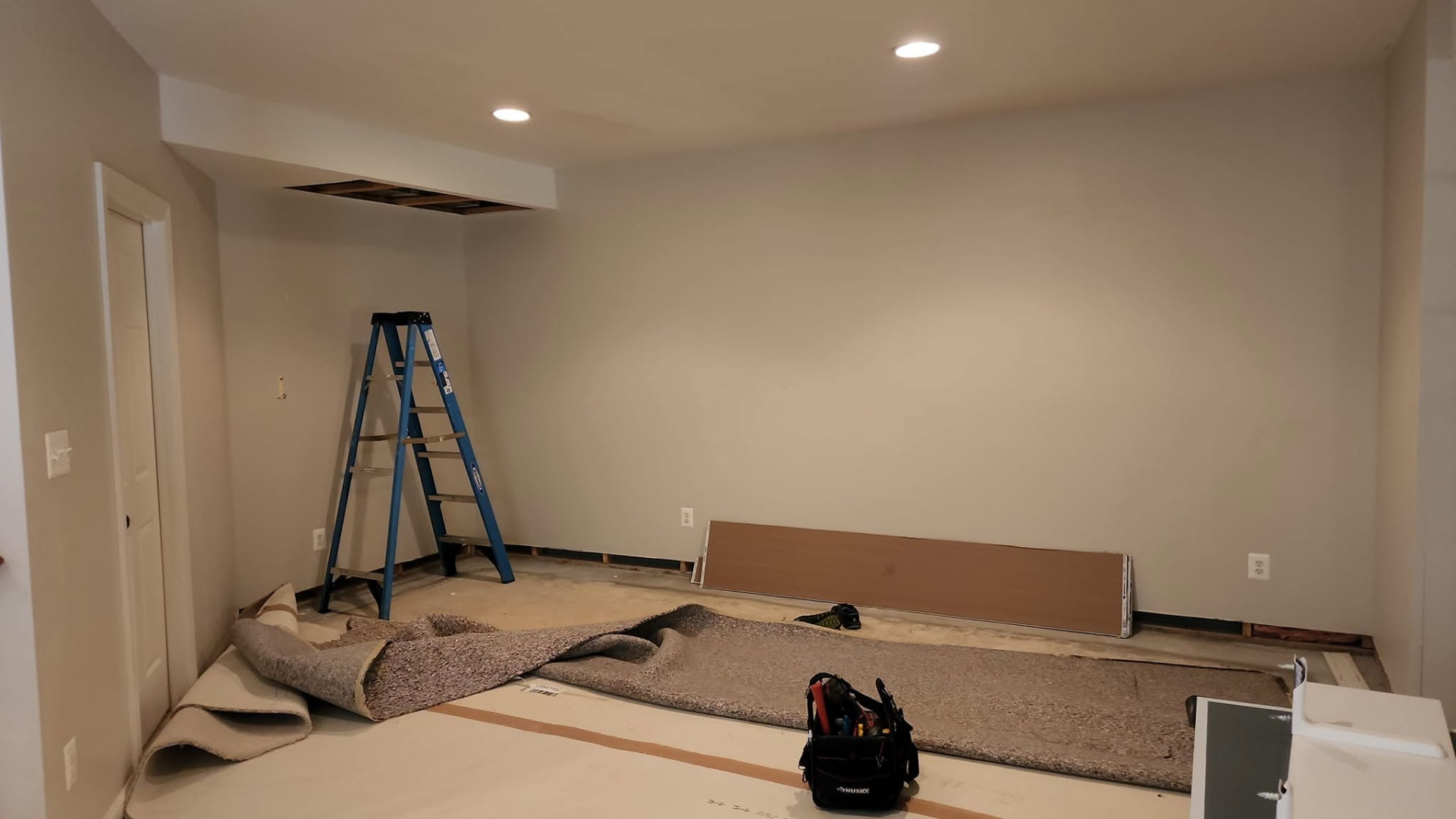 Basement room mid-renovation with carpet pulled and new recessed lights